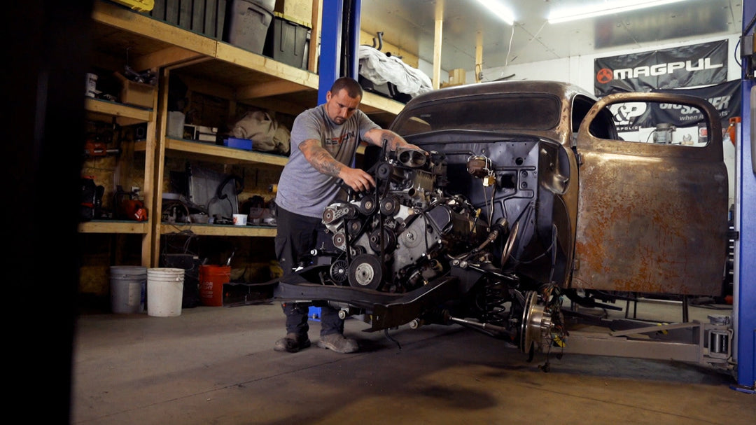 A builder wrenching on a custom truck engine and bare chassis in the Devon Built garage