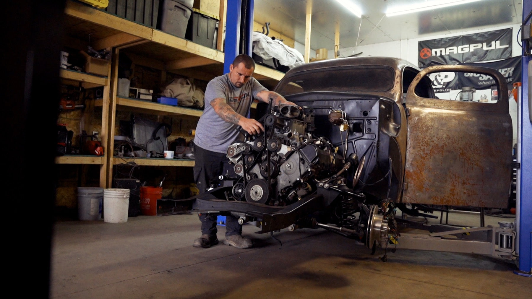 A builder wrenching on a custom truck engine and bare chassis in the Devon Built garage
